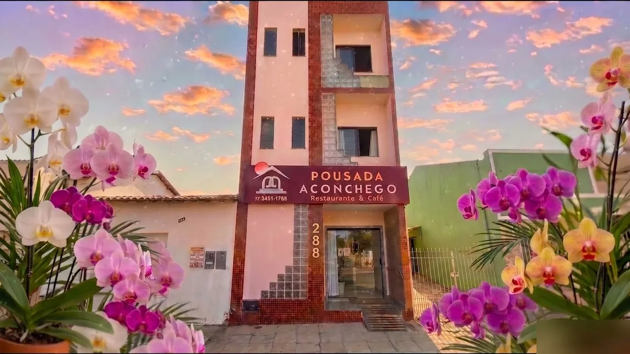 Fachada da Pousada Aconchego ao entardecer, emoldurada por orquídeas — Praça da Bandeira, Poções, Bahia